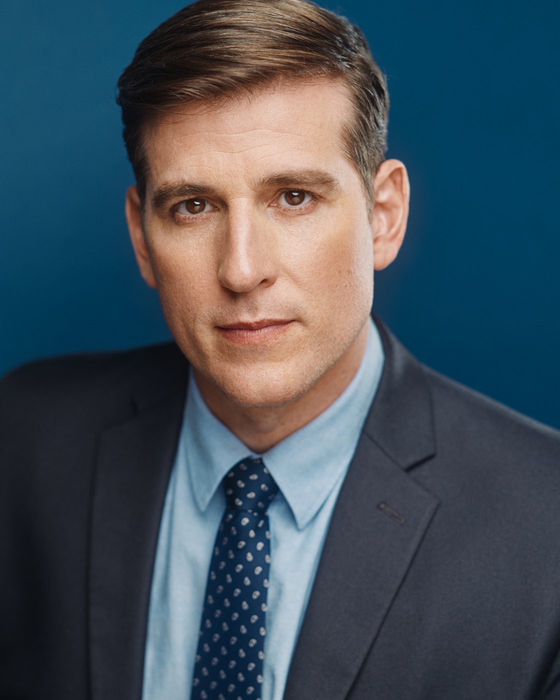 Jonathan Chase Greenfield in a suit and tie against a blue background